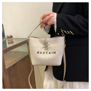 Detail of woven bucket bag with black RESTAIN embroidery and elegant metal buckle closure