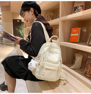 Detail view of cream nylon backpack with cute bear pendant and multi-zipper pockets