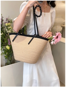 Détail d'un grand sac cabas tissé beige avec poignées noires porté par un mannequin