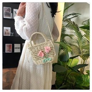 Elegant woven straw bag with pink tulip detail shown on a stylish summer dress