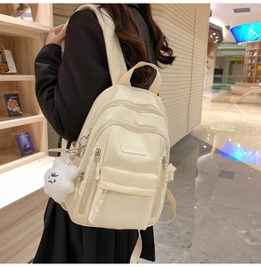 Close-up of beige waterproof backpack with multi-layer zipper pockets and a cute plush charm