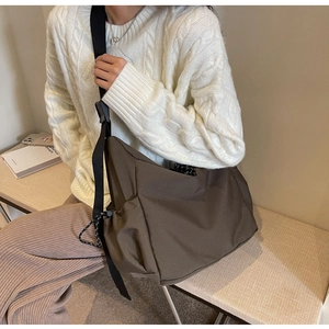 Detail of a large coffee brown messenger bag with adjustable strap worn by a model