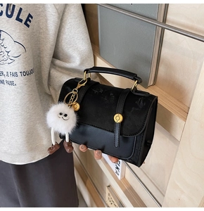 Detail of black faux leather handbag with suede patchwork and white plush charm