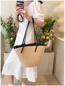 Détail d'un sac cabas en paille tissée avec anses noires porté sur une robe blanche