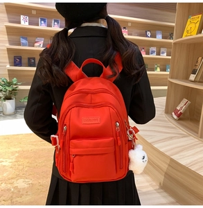 Close-up of vibrant red nylon backpack with zipper layers and a cute white plush charm