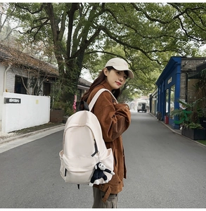 Side view of cream nylon backpack on model featuring a black plush monkey keychain