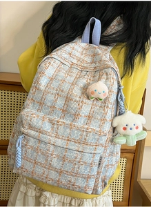 Close-up of blue and orange checkered corduroy backpack with peach patch and plush puppy charm