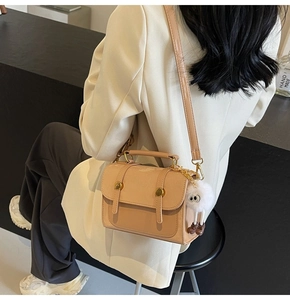 Detail view of beige PU leather handbag with plush doll charm and gold hardware accents