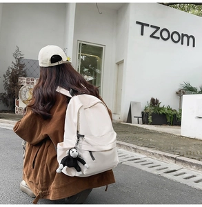 Outdoor street view of a cream nylon backpack featuring a cute black plush monkey keychain