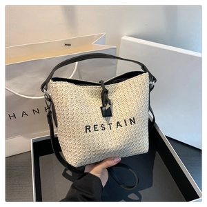 Minimalist straw bucket bag with black leather straps and embroidered RESTAIN lettering