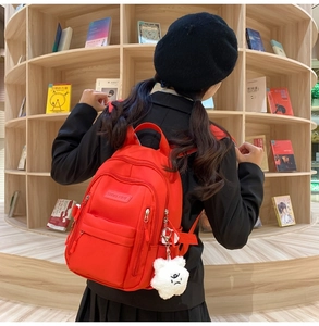Close-up of red waterproof nylon backpack with zipper pockets and a plush doll pendant