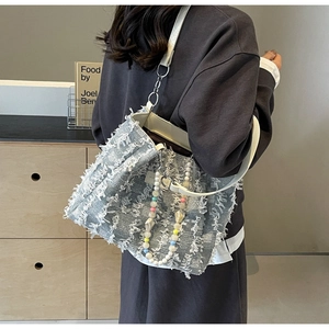 Detailansicht der graublauen Tweed-Tasche mit Fransenstruktur und dekorativer Perlenkette