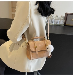 Detail of beige minimalist faux leather bag with gold lock and plush charm on shoulder