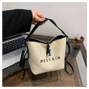Sac seau minimaliste en paille avec broderie RESTAIN noire et lanières en cuir sur un bureau