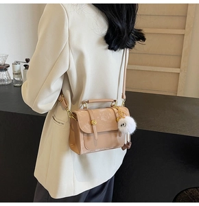 Detail view of beige PU leather crossbody bag with cute plush pendant on a model