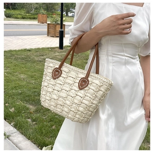 Detailed close-up of woven straw handbag texture and brown leather handle attachment
