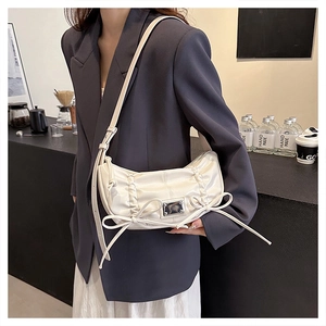 Gros plan d'un sac à bandoulière blanc brillant plissé avec nœuds et plaque en métal