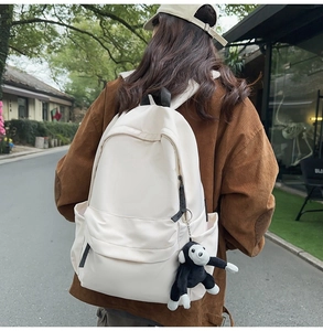 Close-up of cream nylon backpack featuring a front zipper pocket and cute monkey keychain