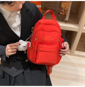 Detail of red nylon backpack with multiple zipper pockets and white plush charm accessory