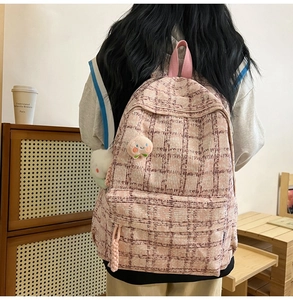 Close-up of pink corduroy backpack with grid pattern and cute plush peach pendant