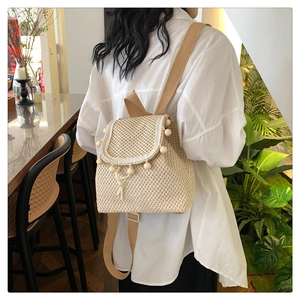 Detail of beige woven straw backpack featuring wooden bead trim and fabric shoulder strap
