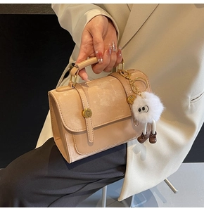 Detail of light khaki PU handbag with gold metal buckles and a cute plush monster charm