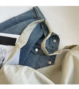 Detail view of stylish beige canvas crossbody bag with wide strap on denim jacket