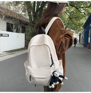 Outdoor model wearing a minimalist beige nylon backpack with a cute monkey plush charm