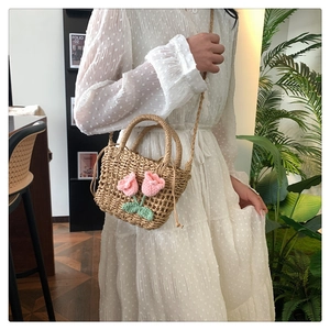 Detail of hand-woven straw bag with pink crochet tulip decor worn by a model