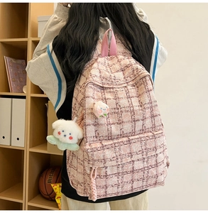 Detail of pink and white plaid tweed backpack with cute plush dog and peach charms