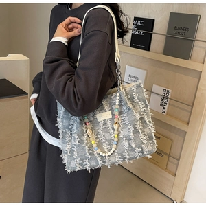 Detail einer hellblauen Tweed-Tasche mit Fransen und Perlen-Muschel-Anhänger-Griff