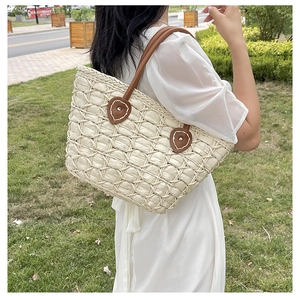 Detail of leaf-shaped leather patch and woven straw texture on women's tote bag