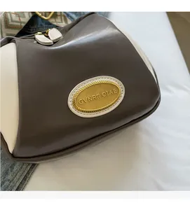 Detail der hochwertigen Nähte, goldenen Logo-Plakette und des gemusterten Webgurts der Tasche