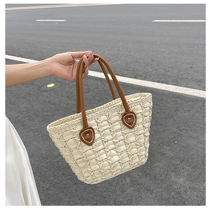 Close-up of woven beige tote bag featuring brown leather handles and metal hardware detail