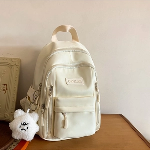 Minimalist off-white backpack in PU leather with plush star charm on a wooden surface