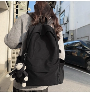 Detail view of a black nylon backpack with a decorative monkey pendant and side pockets