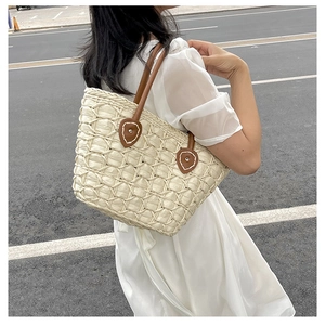 Detail of hand-woven straw tote bag with brown leather handles worn by a model
