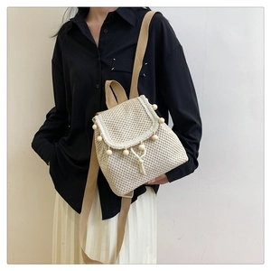 Detail of cream woven backpack showing textured knit fabric and decorative pom-pom trim