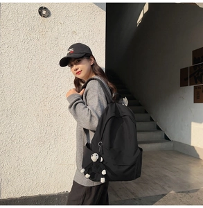 Outdoor shot of a black nylon backpack with front pocket and plush monkey charm