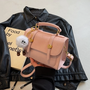 Chic pink PU leather handbag with gold accents and a plush monster charm in hand