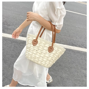 Detail of woven straw tote bag with brown handles and white stitching accents