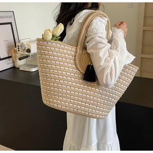 Detail of the large straw woven tote bag featuring beige stripes and a black tassel charm