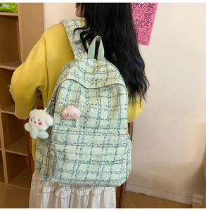 Detail of light green plaid corduroy backpack featuring peach patch and teddy bear charm