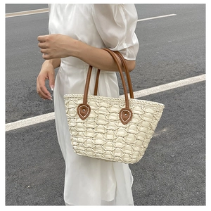 Detailed view of woven straw tote with brown leather handles and stitching