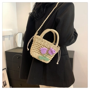 Detailed close-up of handmade straw bucket bag with purple crochet flower and green leaves