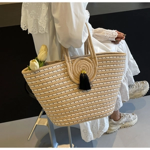 Detail view of woven straw handbag featuring a black tassel charm and tulip decoration
