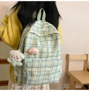 Detail view of light green plaid backpack featuring peach patterns and a white puppy pendant