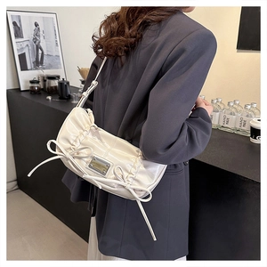 Sac demi-lune en cuir verni crème avec détails nœuds porté à l'épaule élégant