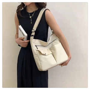 Dettaglio della borsa a tracolla oxford color crema con doppie tasche anteriori a zip