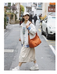 Detailed street view of orange nylon crossbody bag with adjustable wide strap and side pocket